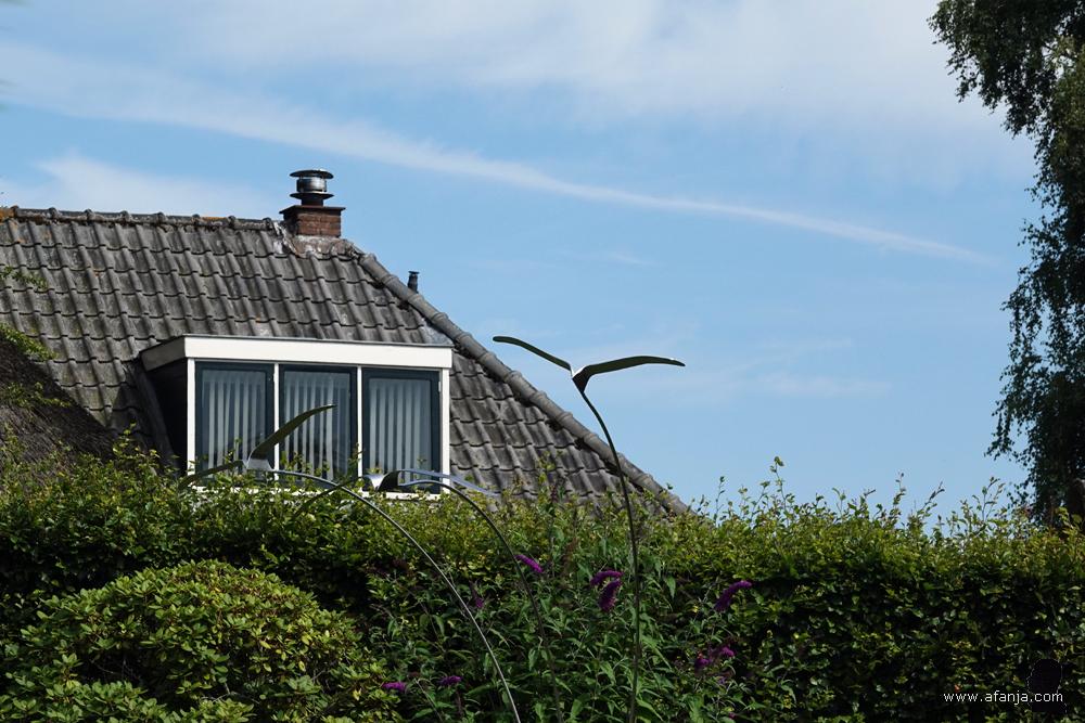 in de tuin staat een kunstinstallatie van drie metalen vogels in de vlucht