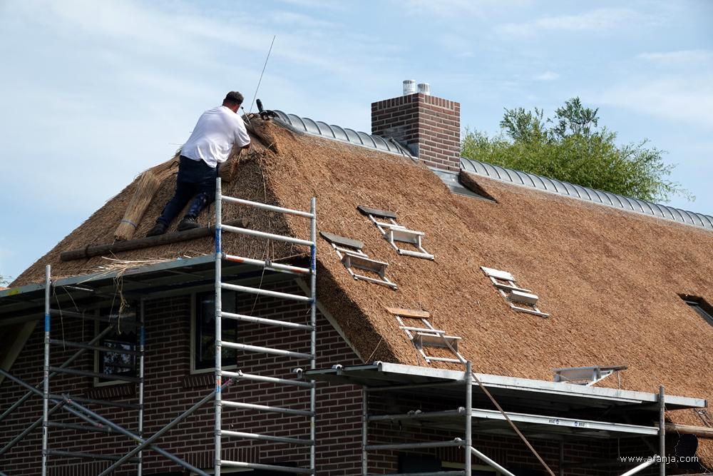 een rietdekker is aan het werk op het dak van een woonboerderij