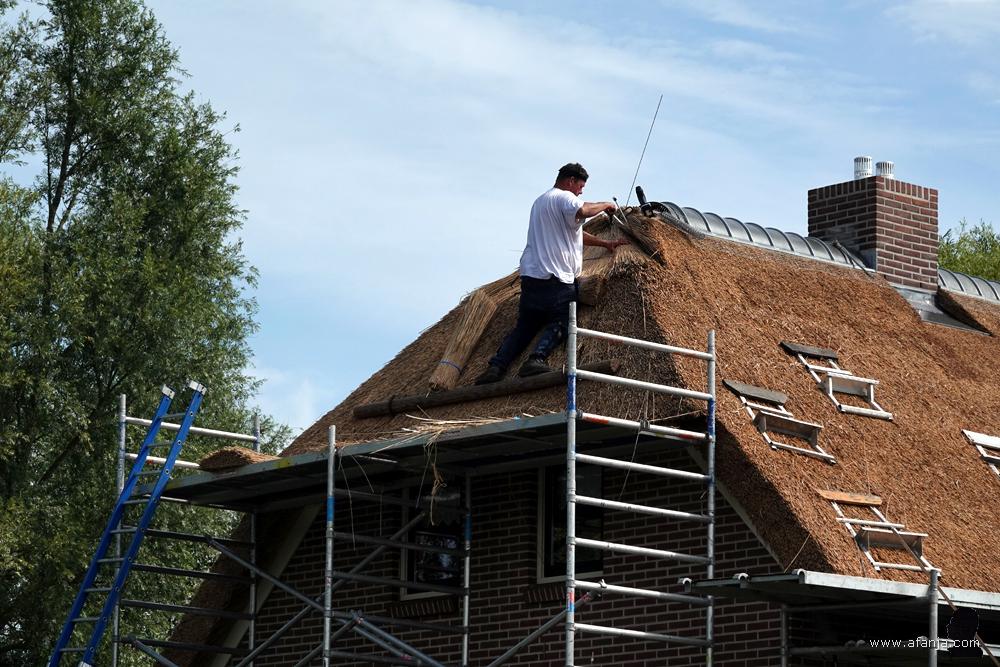 een rietdekker is aan het werk op het dak van een woonboerderij