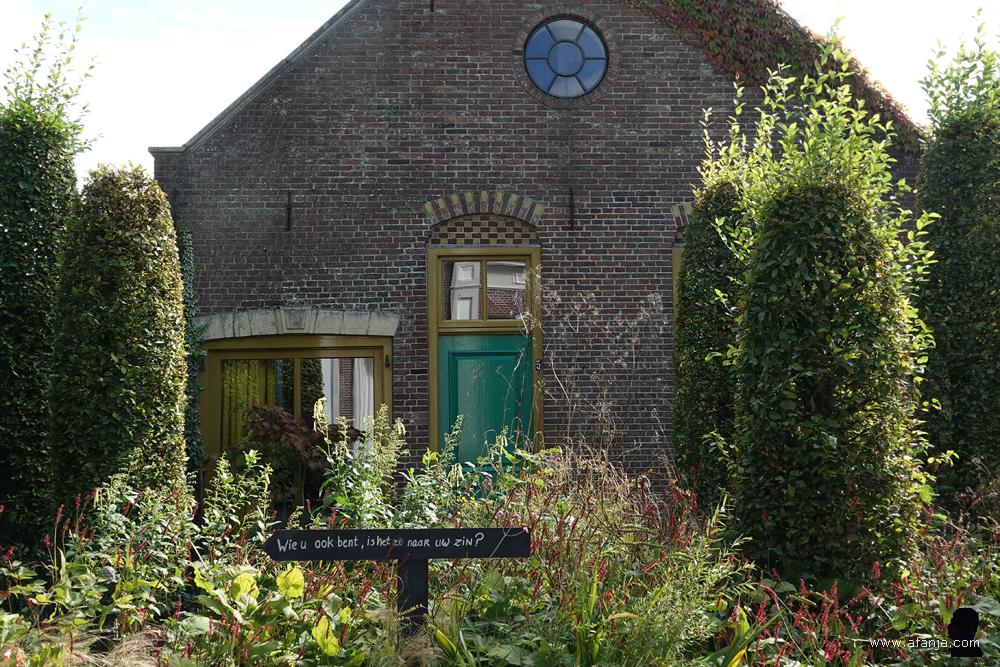 in de tuin staat een bordje met het opschrift 'Wie u ook bent, is het zo naar uw zin?'