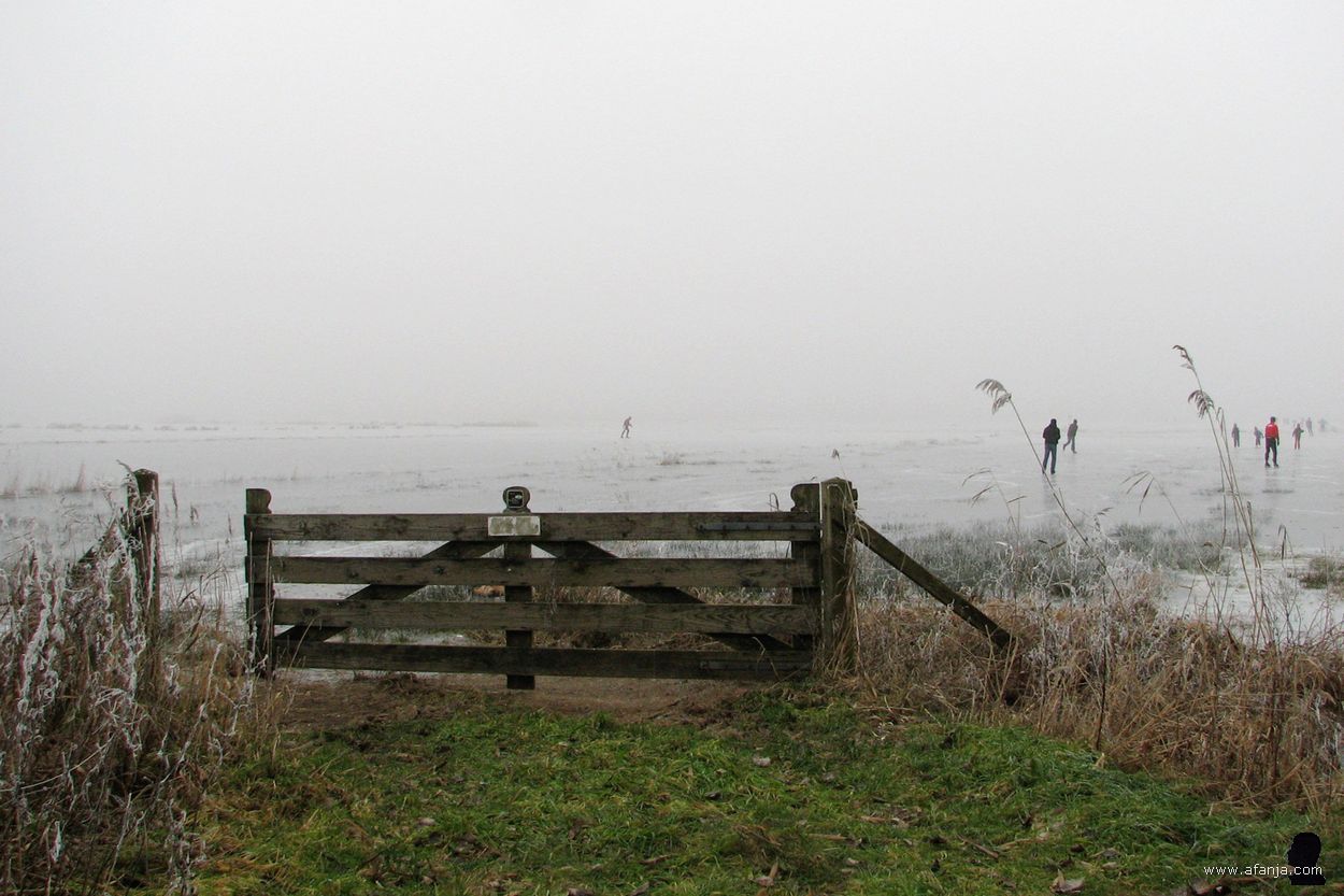 21 december 2007 - een hek met daarachter schaatsers in de mist