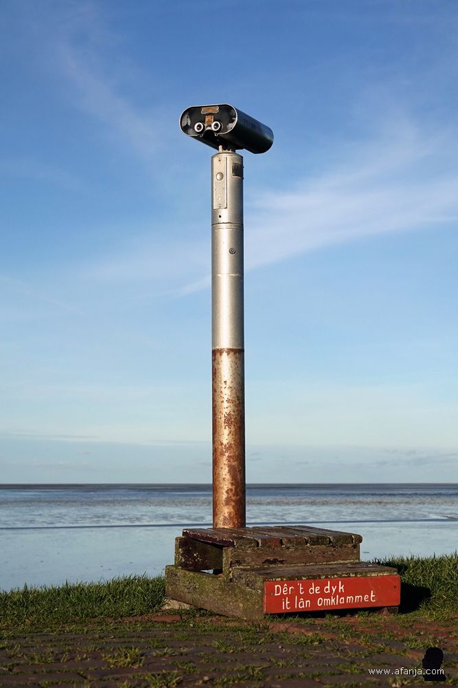 verrekijker met daaronder de tekst 'Dêr't de dyk it lân omklammet' - 'Waar de dijk het land omhelst'