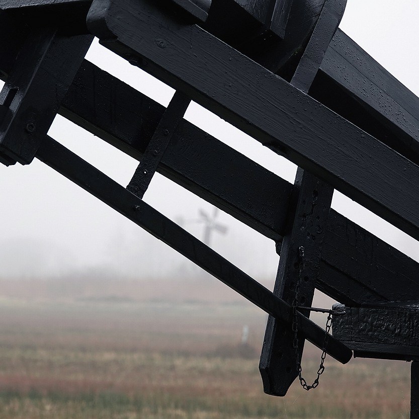 op de achtergrond vaag zichtbaar een kleine windmotor in de mist, op de voorgrond een deel van de tjasker
