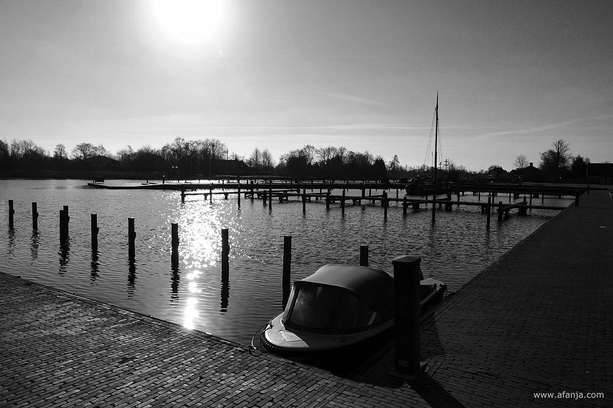 zwart/wit foto van een klein bootje en op de achtergrond een skûtsje in de jachthaven van Earnewâld