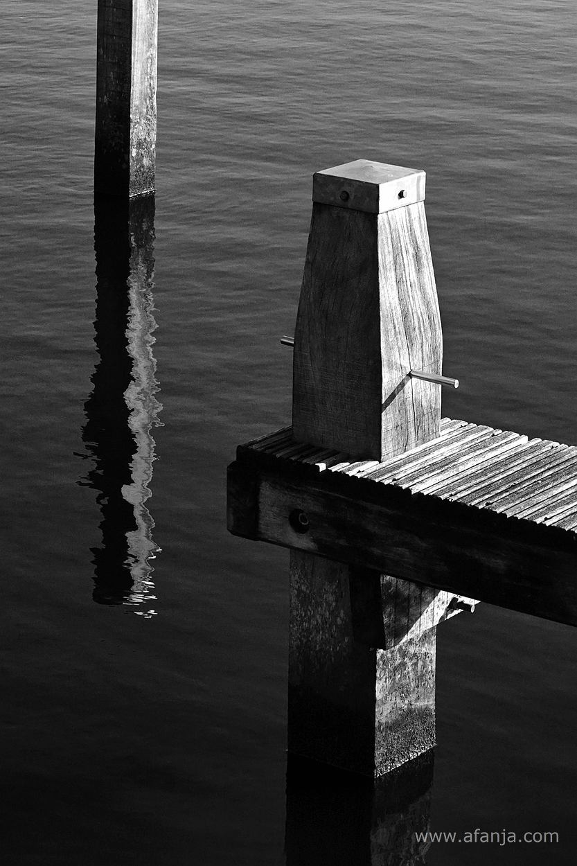 zwart/wit foto van twee meerpalen en een aanlegsteigers in de jachthaven