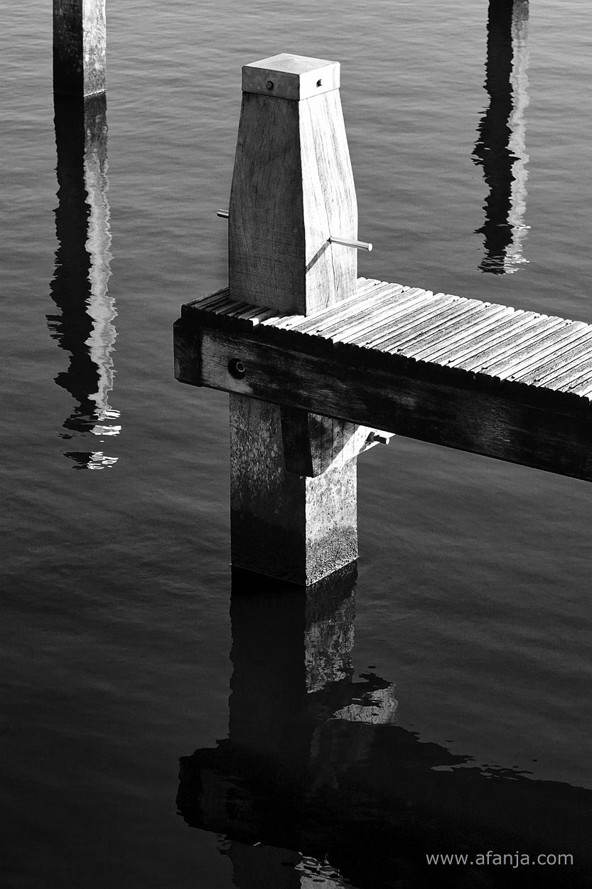 zwart/wit foto van drie meerpalen en een aanlegsteigers in de jachthaven
