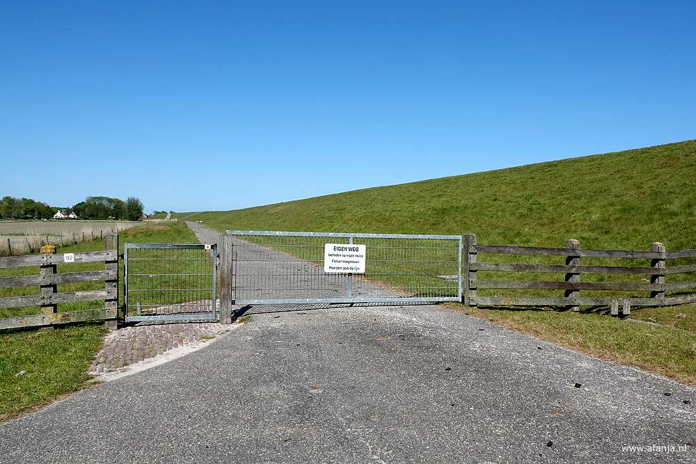 een gesloten hek achter de zeedijk met een bordje