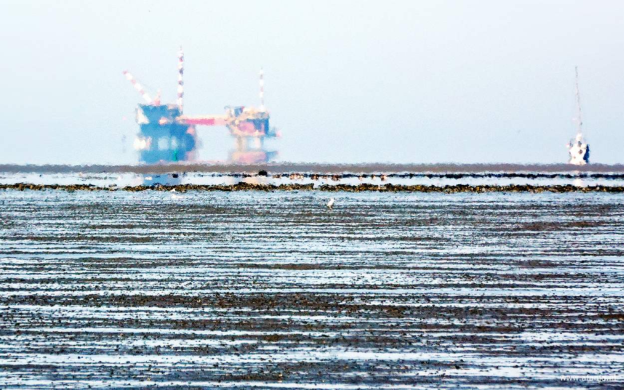 een fata morgana oftewel luchtspiegeling van een boorplatform en een zeilboot aan de horizon