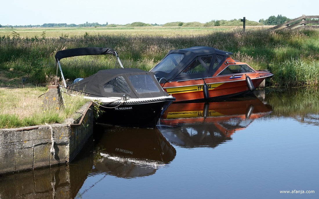 twee kleine motorbootjes met weerspiegeling met op de achtergrond weilanden