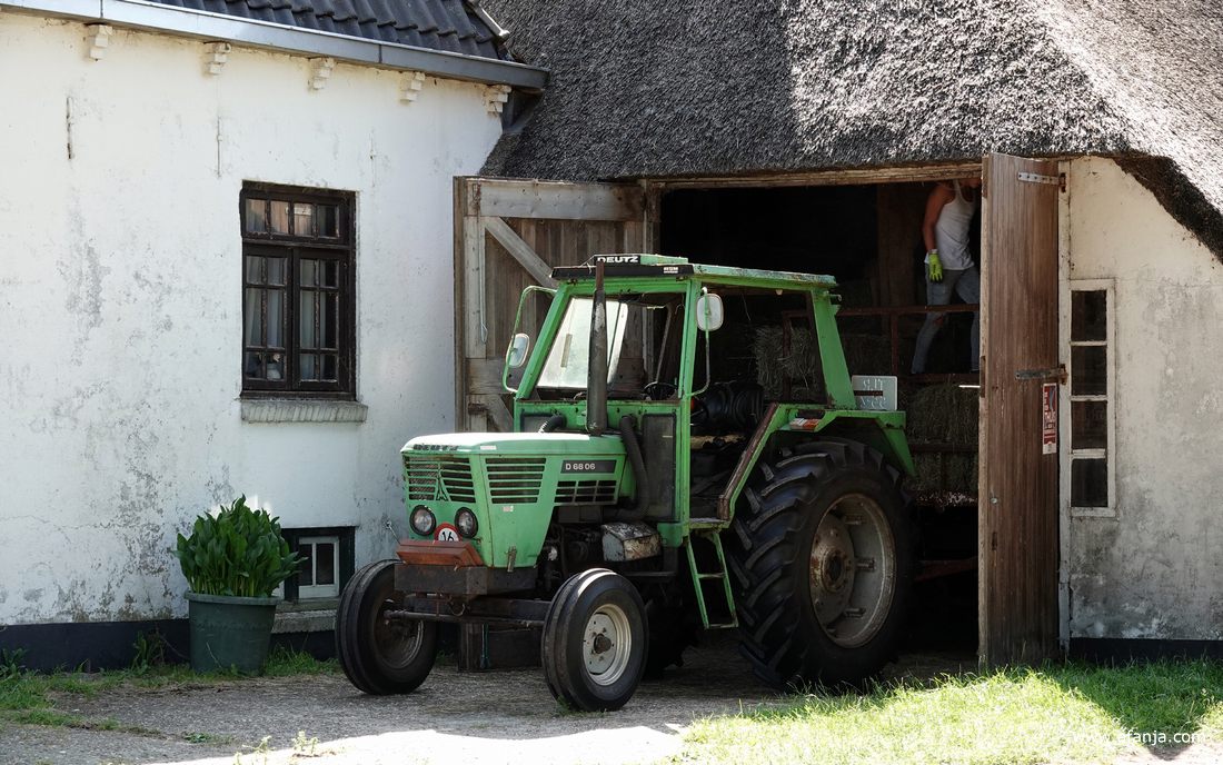 voor de schuur staat een oude trekker, in de schuur worden pakjes hooi uitgeladen