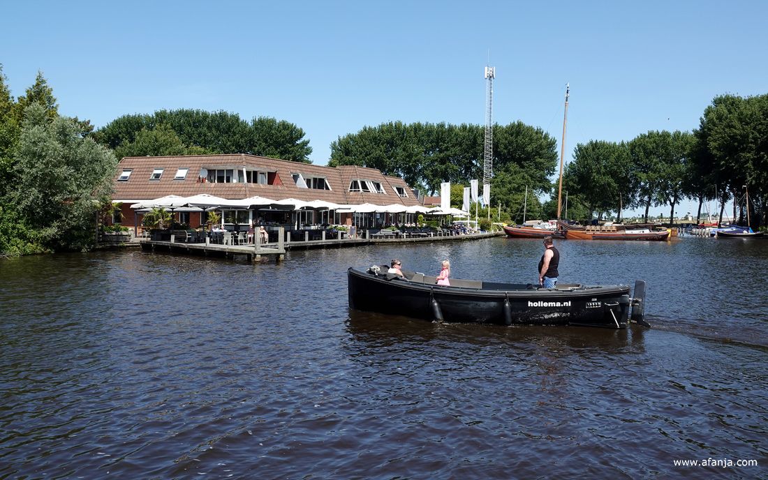 een sloep steekt vlak voor de pont over, op de achtergrond staat hotel-restaurant 'de Hooidammen'