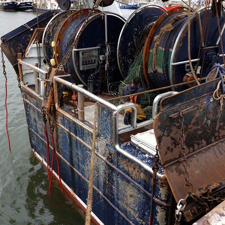 op het achterschip van de UK 642 is een visser netten aan het boeten
