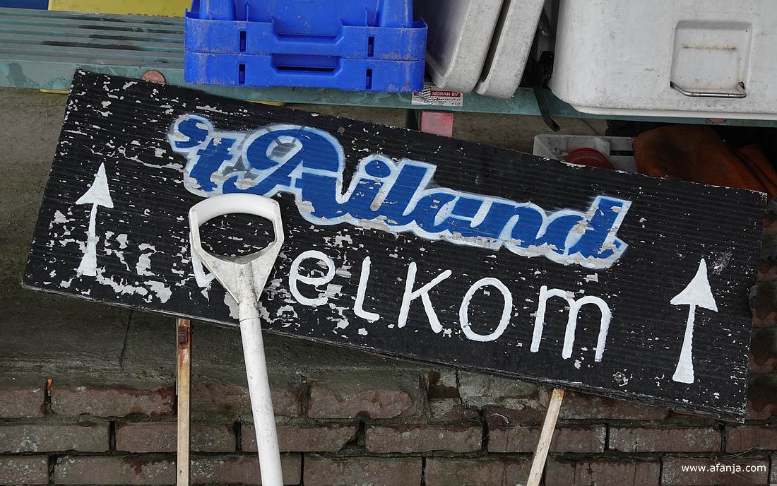 een bord met de tekst "'t Ailand welkom" staat in een rommelig hoekje