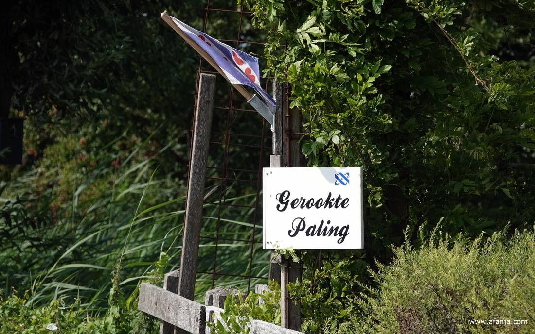 aan een paal hangt onder de Friese vlag een bordje 'Gerookte Paling'