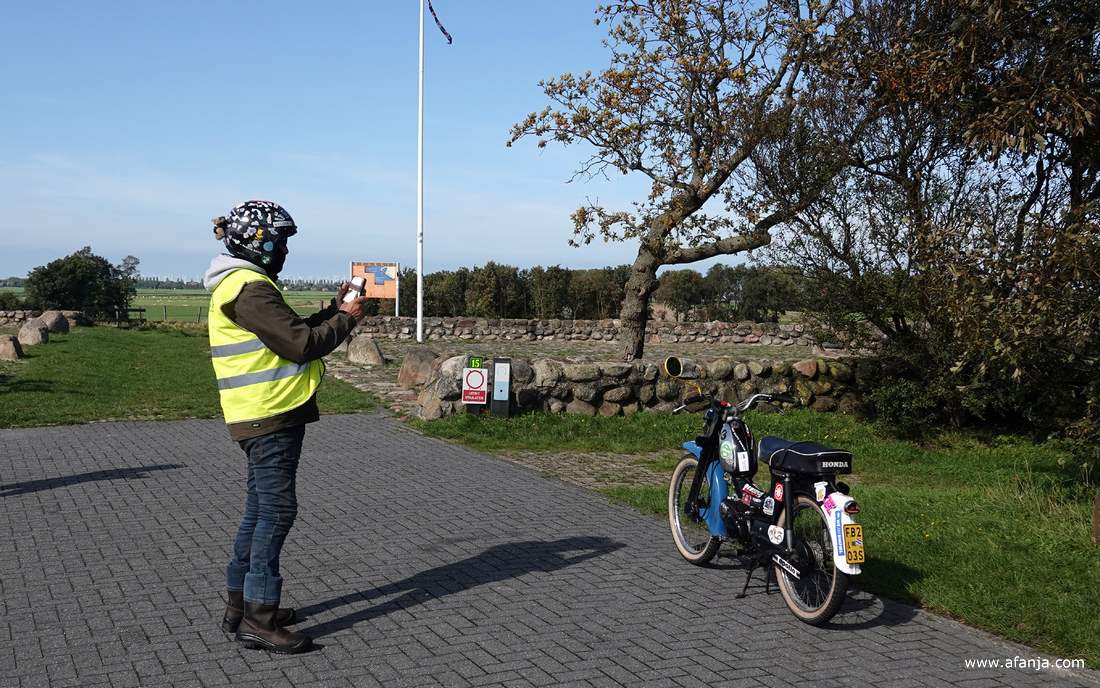 iemand in een geel hesje met een zwarte helm op maakt een foto van een zwart-blauwe Honda brommer die met stickers beplakt is
