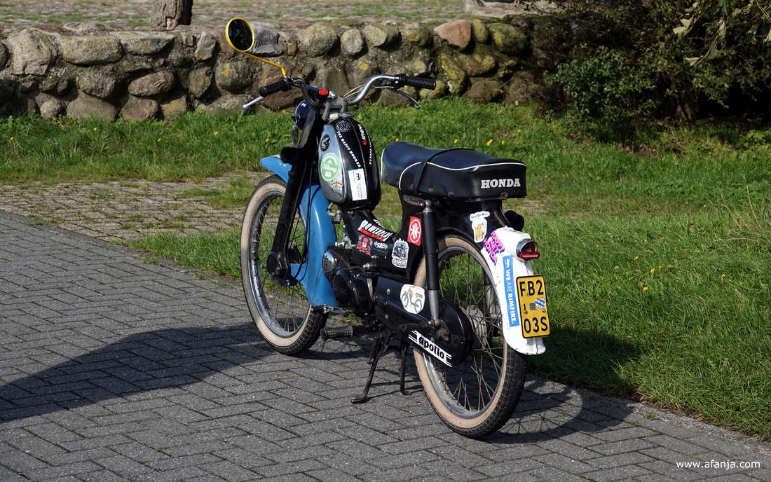 een zwart-blauwe Honda brommer die beplakt is met stickers staat op de standaard