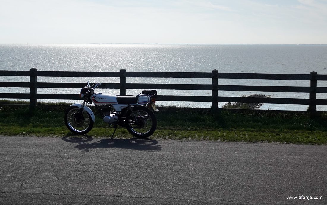 een wart-witte Honda brommer staat bij het hek op Reaklif