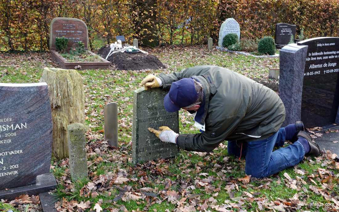 de beheerder wijst op een foutje op een grafsteen