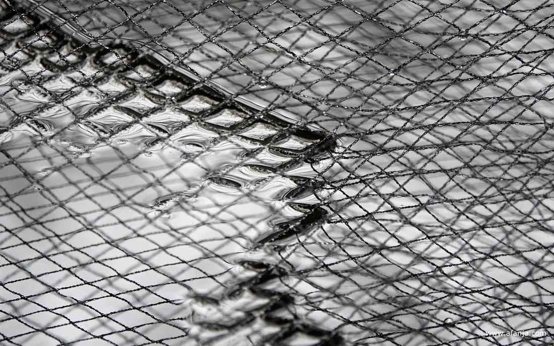 een net, dat over de vijver hangt om bladeren van de hazelaar op te vangen, hangt deels in het water