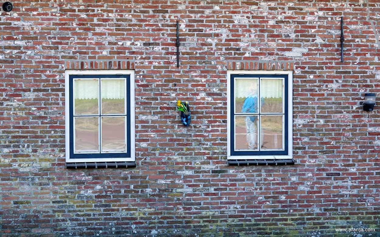 fotomaatje Jetske wordt in haar blauwe jack weerspiegeld in het raam van een oude boerderij