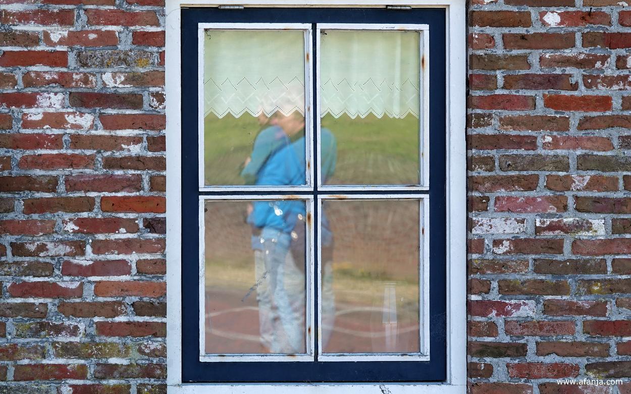 fotomaatje Jetske wordt in haar blauwe jack weerspiegeld in het raam van een oude boerderij